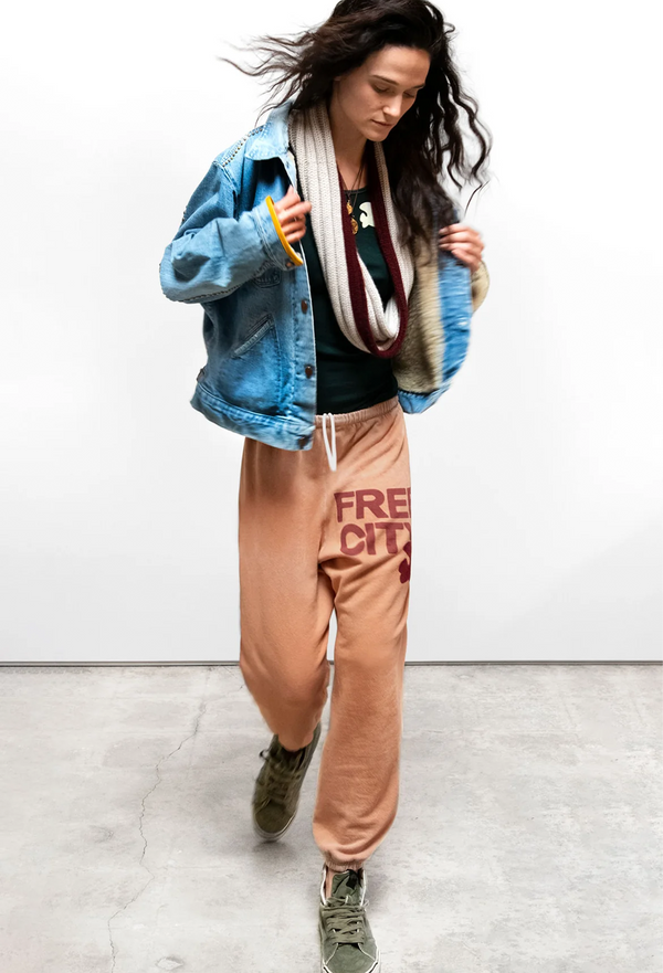 Person wearing a blue denim jacket, orange sweatpants with 'Free City' text, and green sneakers on a white background