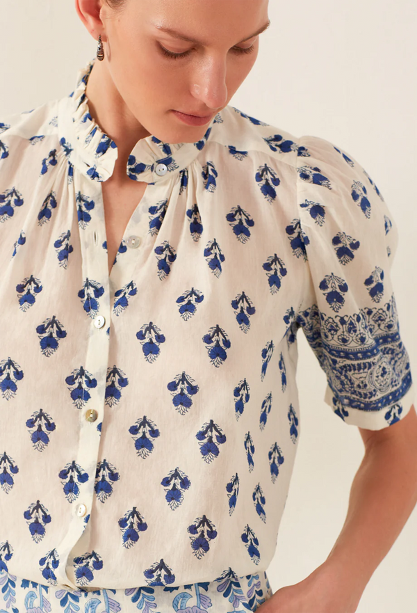 Woman wearing a white blouse with blue floral patterns on a plain background