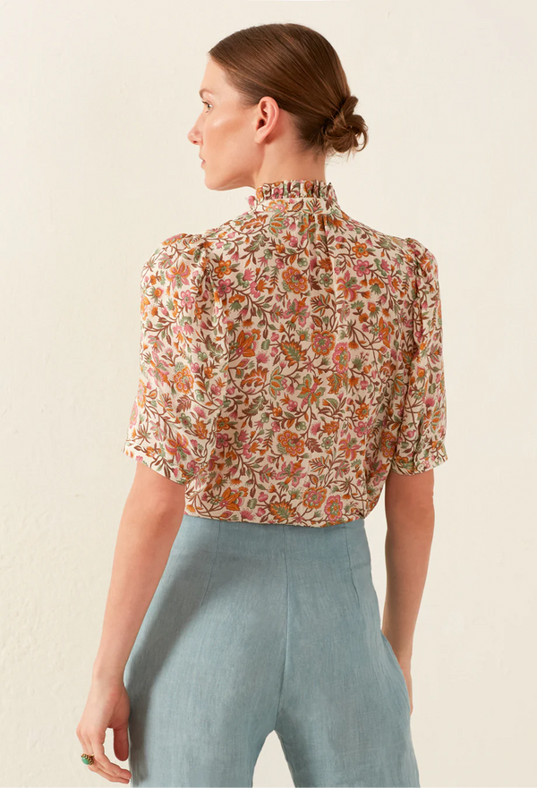 Woman wearing a floral blouse and light blue pants on a beige background