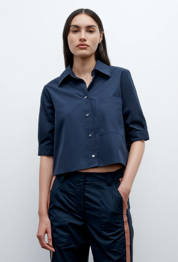 Woman wearing a navy blue cropped button up shirt and pants against a white background