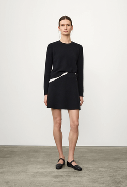 Person wearing a black sweater and black skirt on a plain background