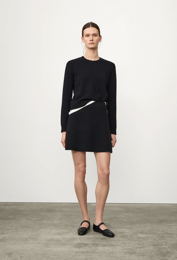 Person wearing a black sweater and black skirt on a plain background