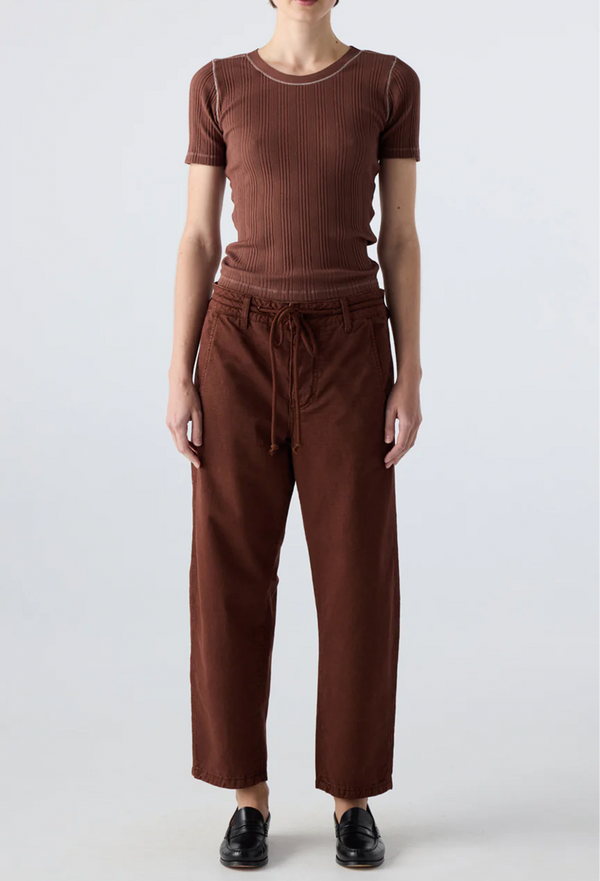 Person wearing a brown ribbed top and drawstring brown pants on a white background
