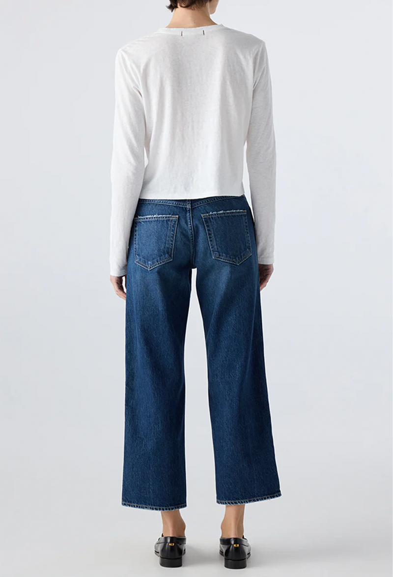 Person wearing a white long-sleeve shirt and blue jeans on a plain background