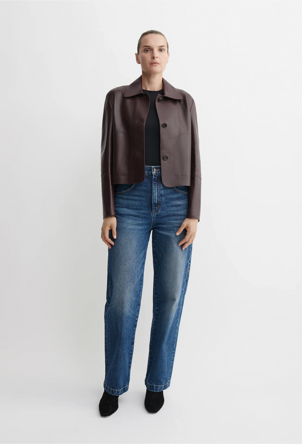 Person wearing a red/brown leather jacket and blue jeans on a white background