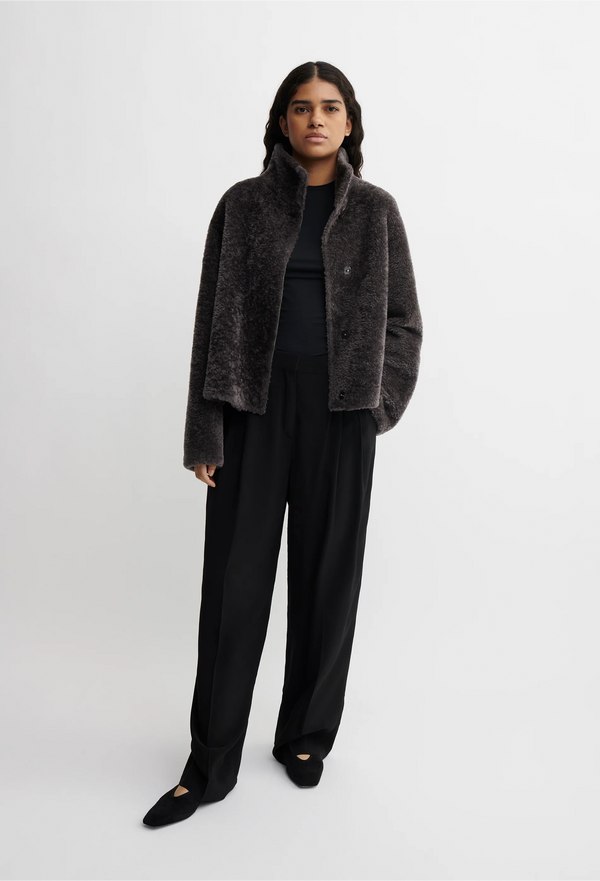 Person wearing a dark gray/brown shearling coat on a white background