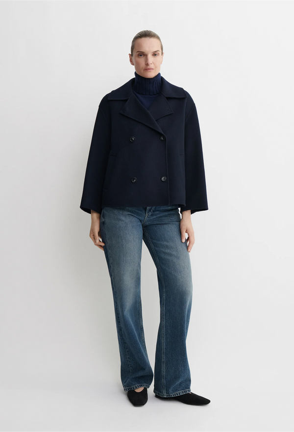 Person wearing a dark blue coat and blue jeans on a white background