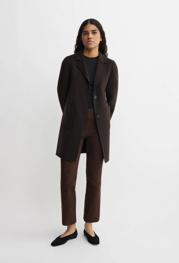 Person wearing a brown long coat and pants on a white background