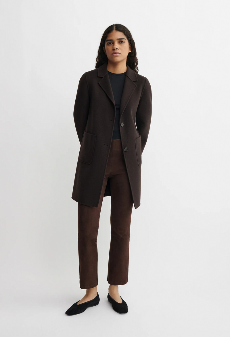 Person wearing a brown long coat and pants on a white background