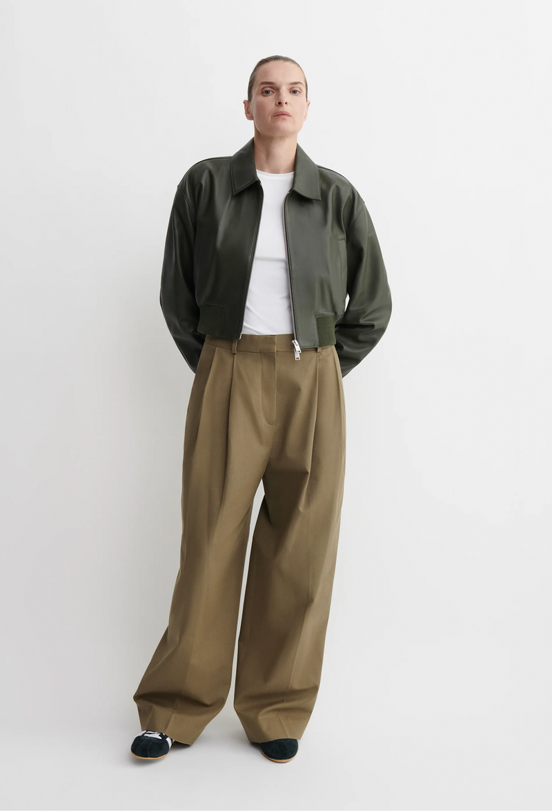Person wearing a green bomber jacket and beige pants on a white background