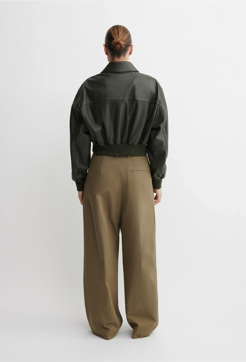 Person wearing a green bomber jacket and beige pants on a white background
