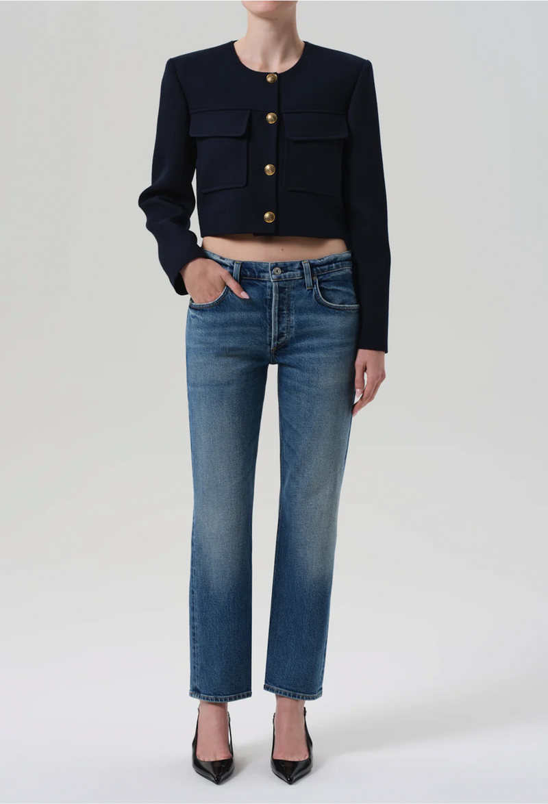 Person wearing a black cropped jacket and blue jeans on a white background