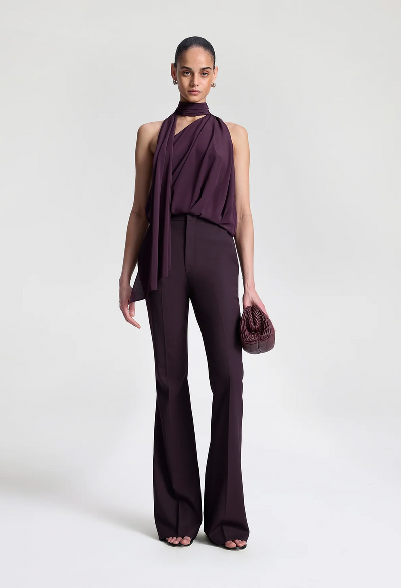 Woman wearing dark purple pants with a matching top on a white background