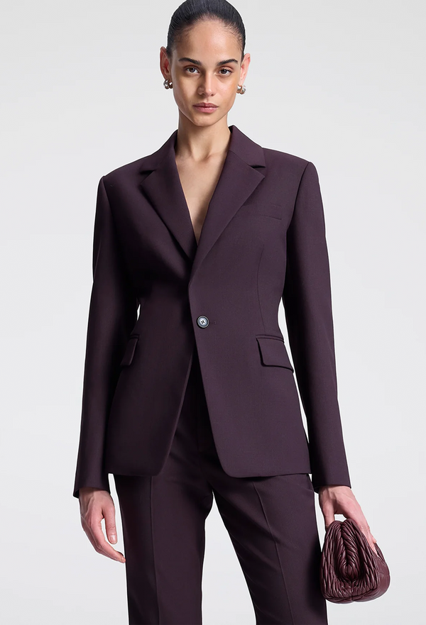 Woman wearing a dark purple suit with a matching handbag on a light gray background