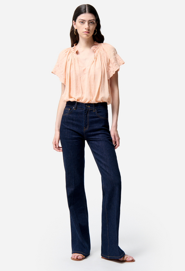Woman wearing a peach blouse and dark blue jeans on a white background