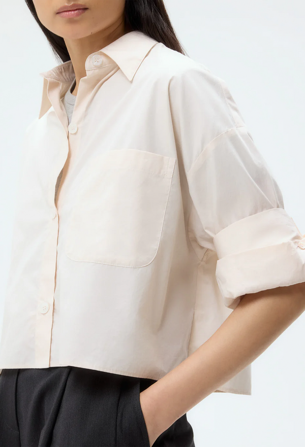 Person wearing a pale pink blouse with rolled-up sleeves on a white background