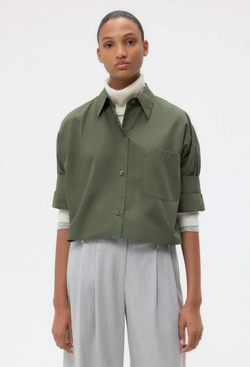 Person wearing a green button down shirt and light gray pants on a white background