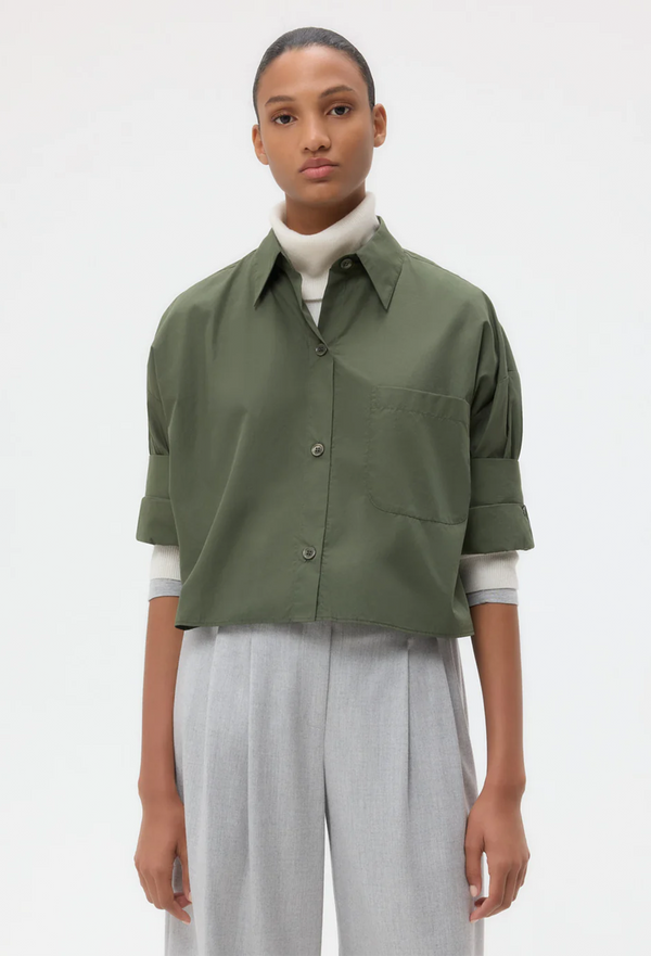 Person wearing a green button down shirt and light gray pants on a white background
