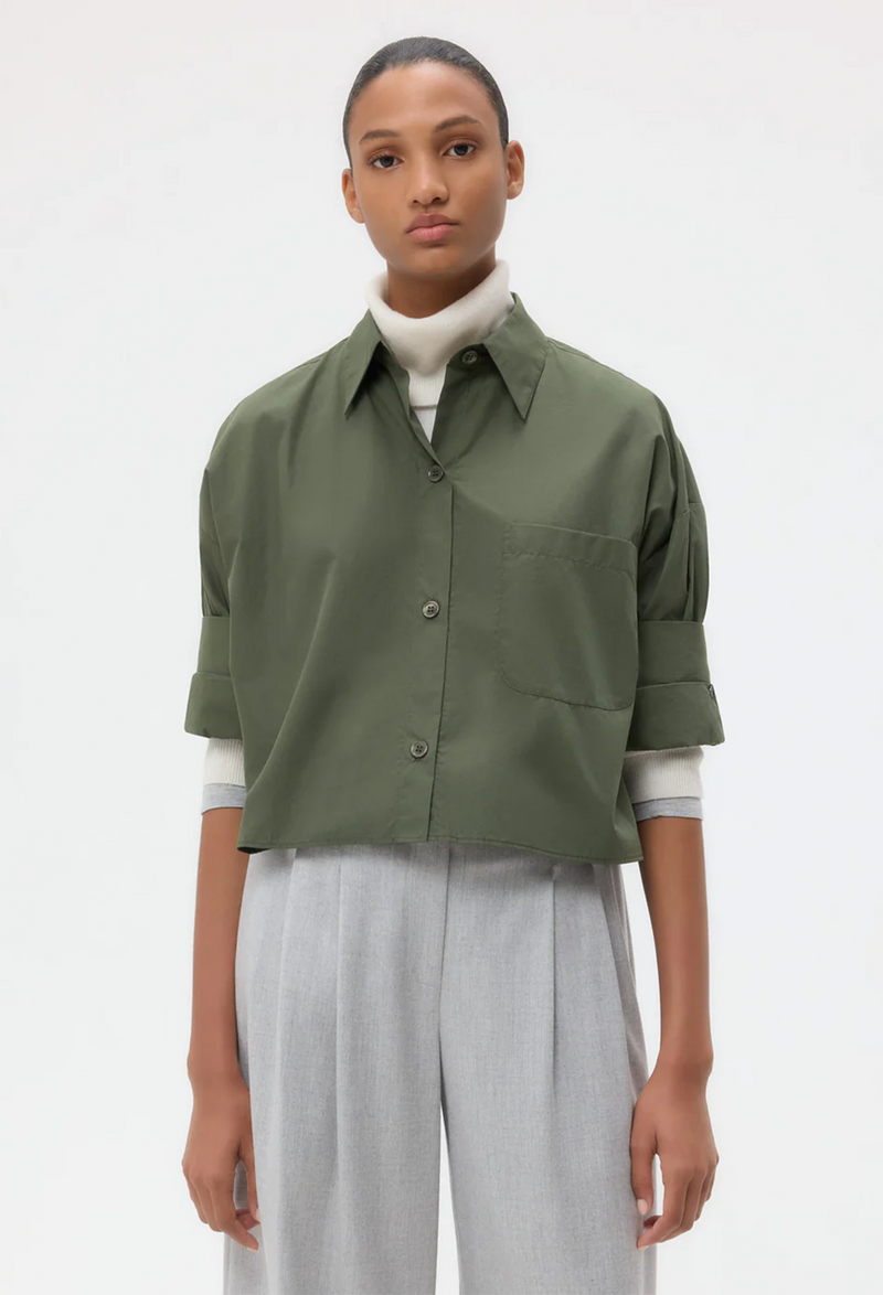Person wearing a green button down shirt and light gray pants on a white background