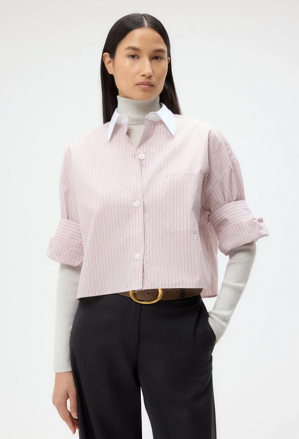 Woman wearing a pink striped button down shirt with rolled-up sleeves on a white background