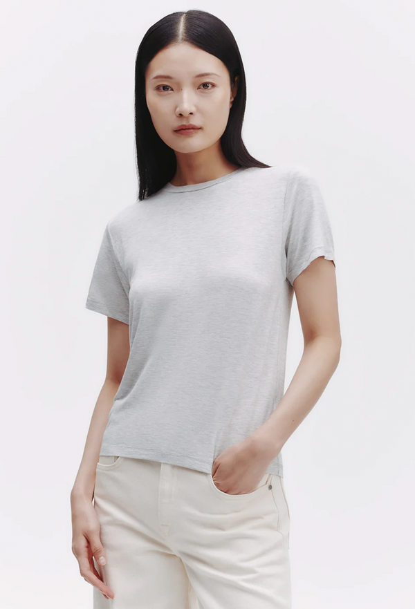 Woman wearing a light heather gray t-shirt and white pants on a plain background