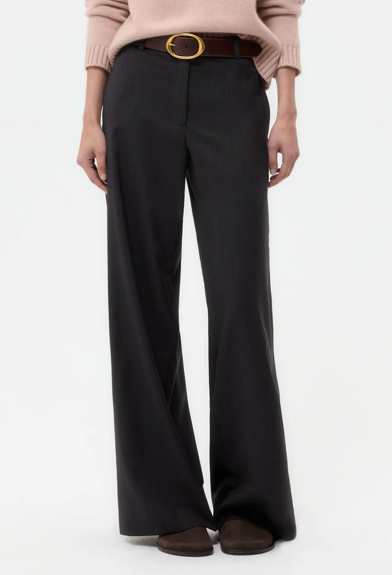 Person wearing charcoal pants with a brown belt on a white background