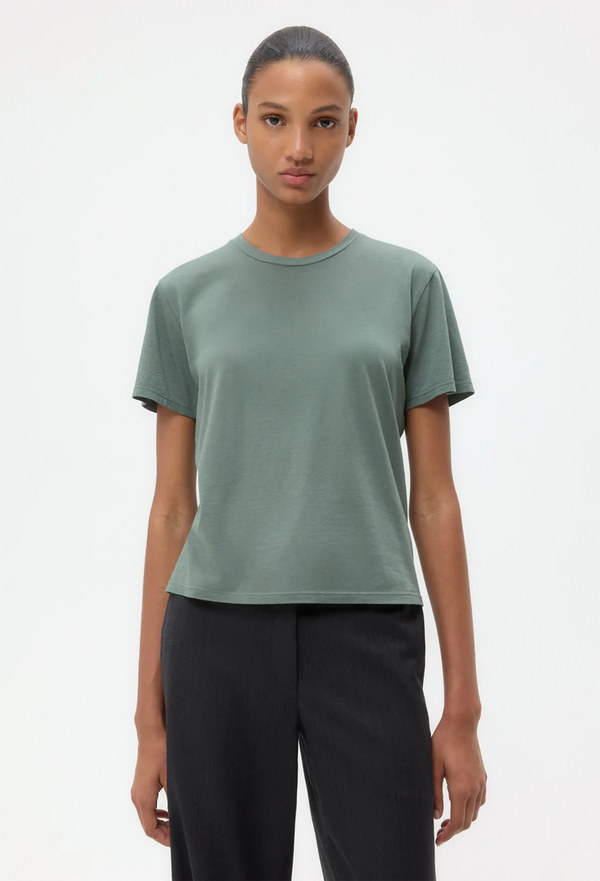 Person wearing a green t-shirt and black pants on a white background