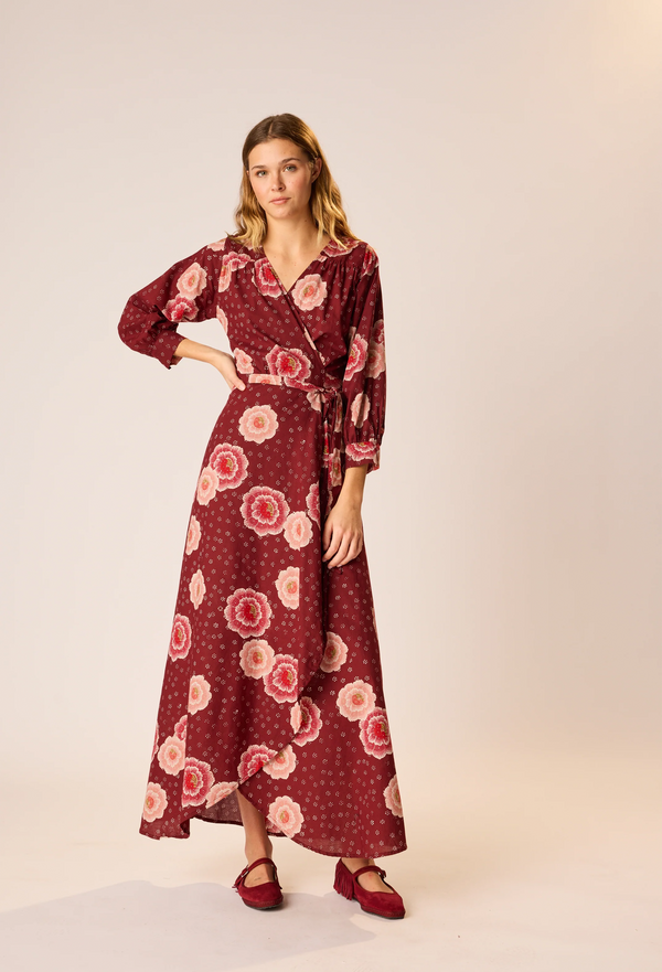 Woman wearing a burgundy wrap maxi dress with floral pattern on a neutral background