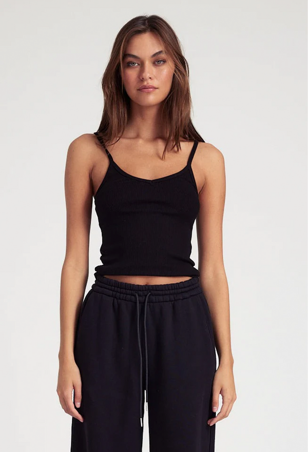 Woman wearing a black v-neck ribbed tank top and black pants on a white background