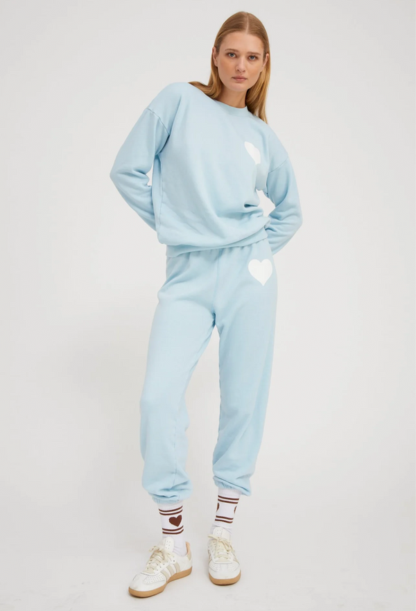 Person wearing a light blue sweatshirt and sweatpants with a white heart design on a white background
