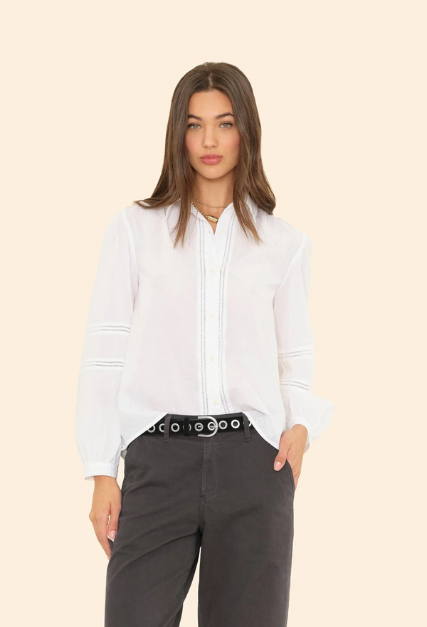 Woman wearing a white long sleeve blouse and black pants on a beige background