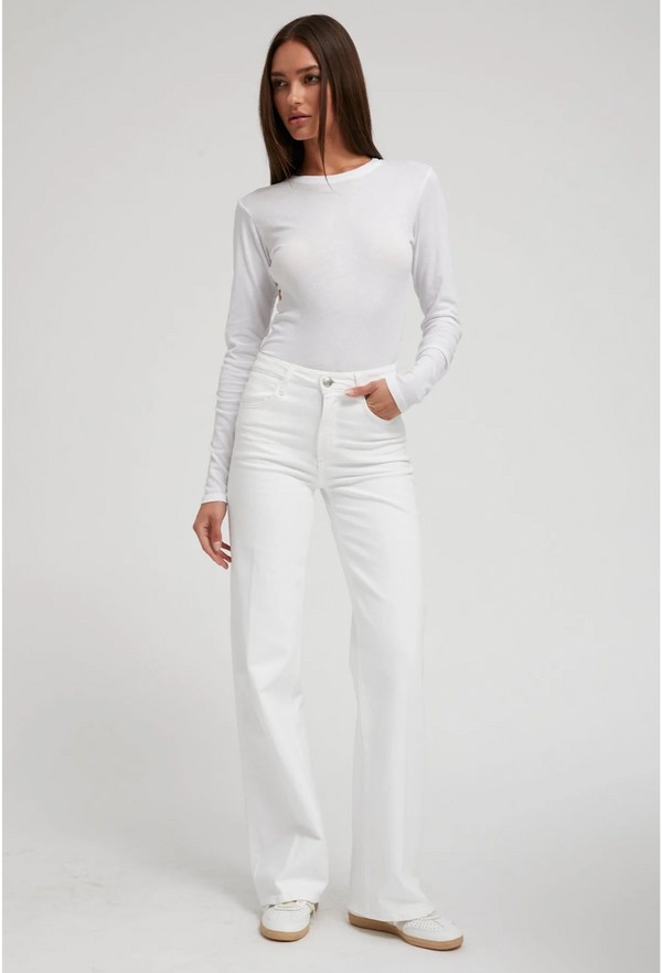Woman wearing a white long-sleeve tee and white jeans on a plain background