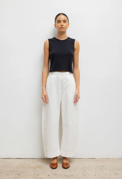 Woman wearing a black sleeveless top and white barrel leg pants on a plain background