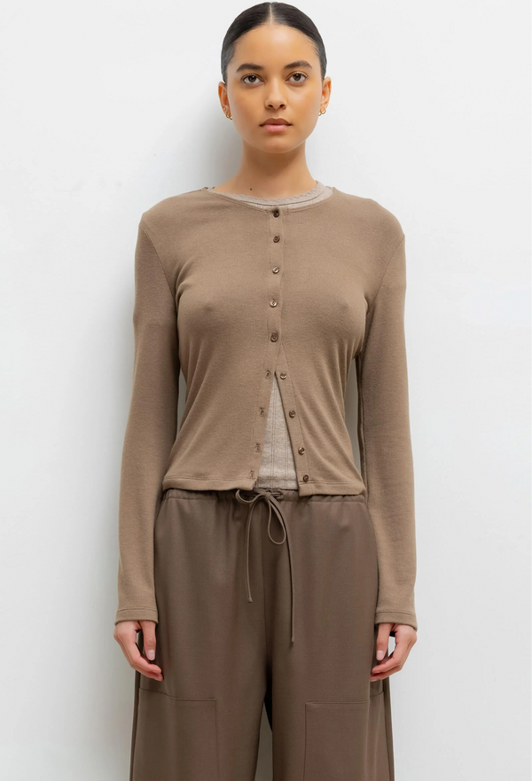 Woman wearing a light brown long-sleeve cardigan and pants on a white background