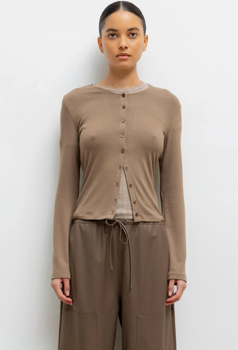 Woman wearing a light brown long-sleeve cardigan and pants on a white background
