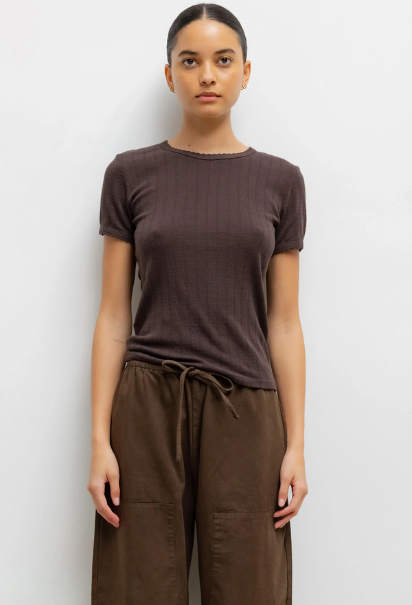 Woman wearing a brown pointelle slim t-shirt and brown pants against a white background