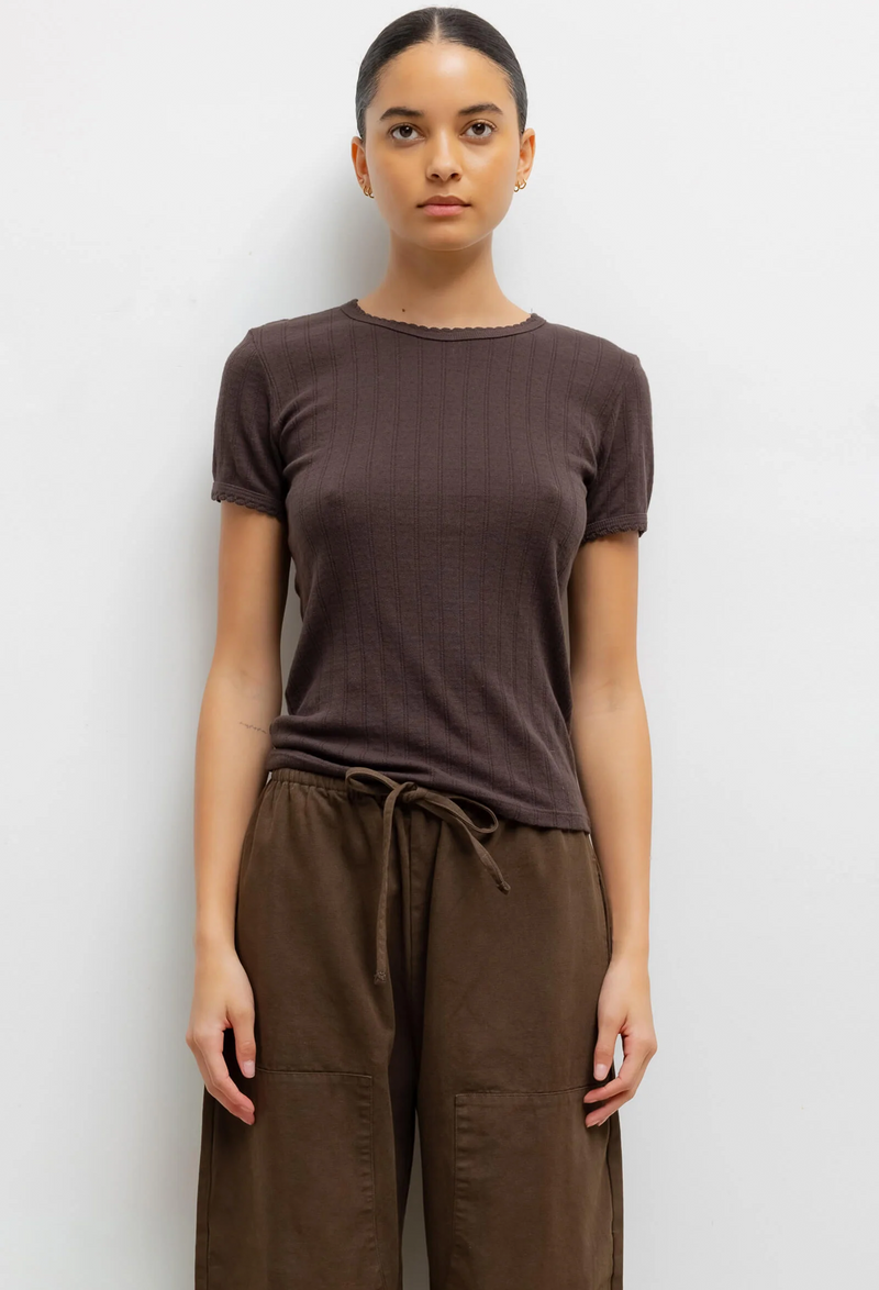 Woman wearing a brown pointelle slim t-shirt and brown pants against a white background