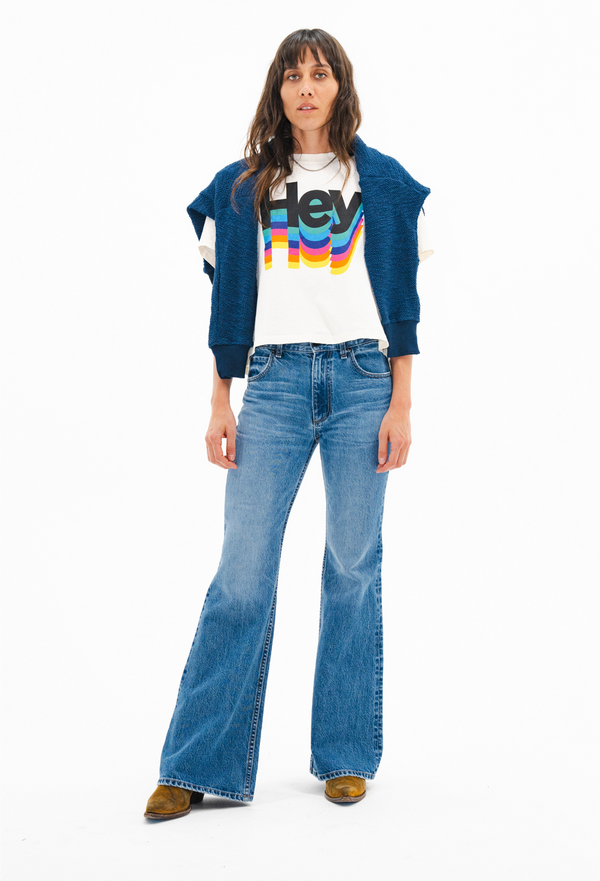 Person wearing a blue cardigan, white t-shirt with colorful text, and blue jeans on a white background
