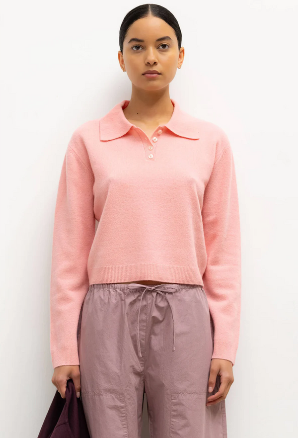 Woman wearing a pink long-sleeve polo shirt and brown pants against a white background
