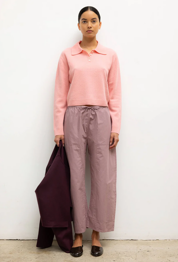 Person wearing a pink sweater and light purple pants against a white wall