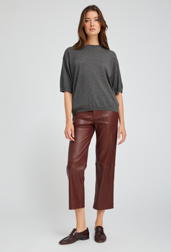 Woman wearing a gray sweater and burgundy leather pants on a white background