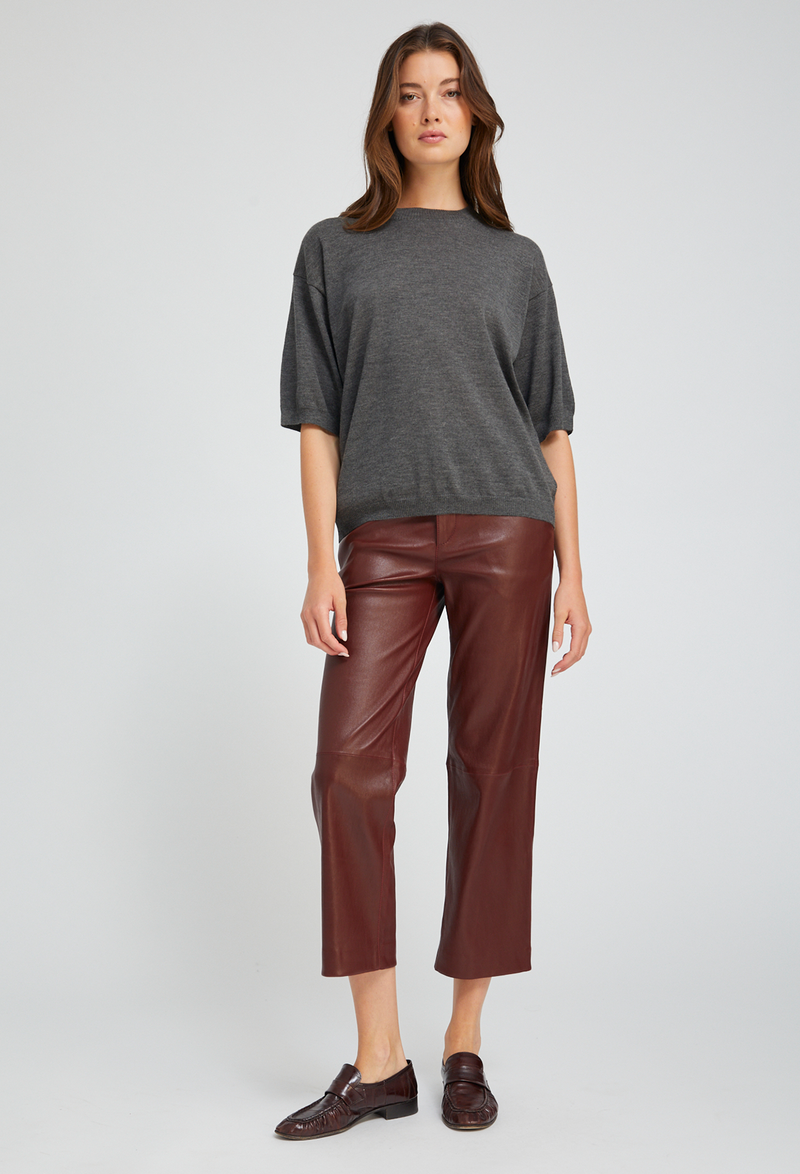 Woman wearing a gray sweater and burgundy leather pants on a white background