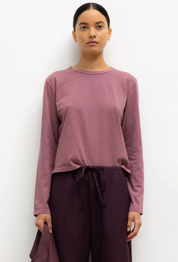 Woman wearing a mauve long-sleeve top and dark purple pants against a white background
