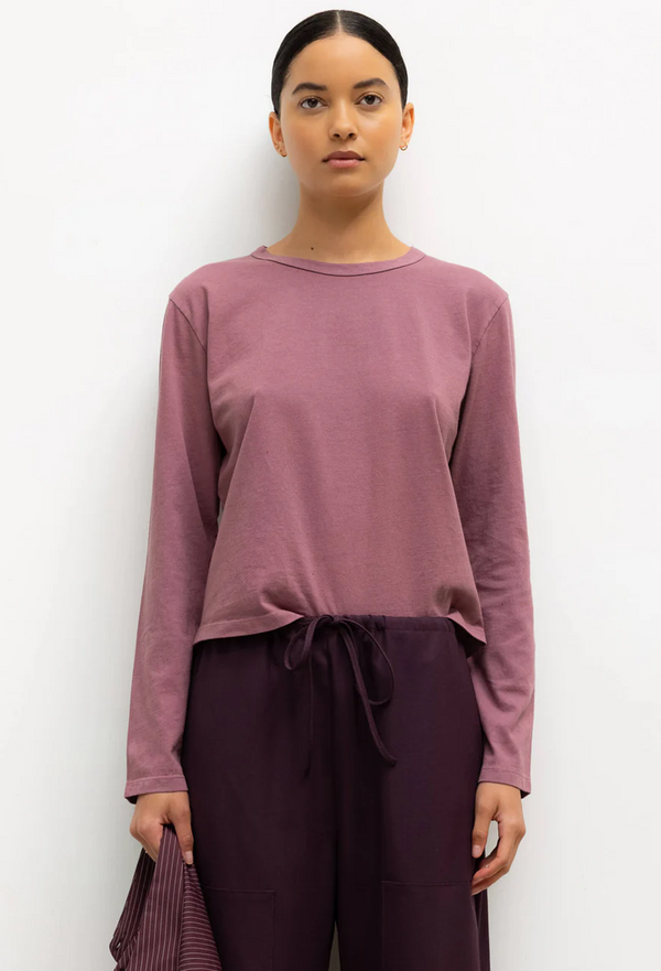 Woman wearing a mauve long-sleeve top and dark purple pants against a white background