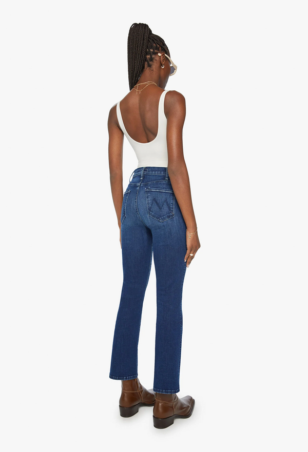 the back of a woman wearing a white tank top and high rise ankle length dark blue jeans. white background