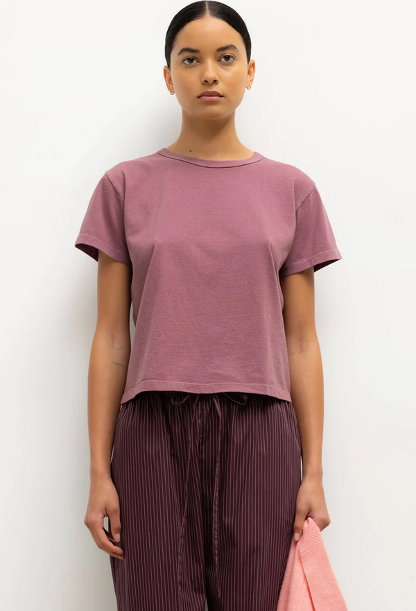 Person wearing a mauve t-shirt and maroon pants against a white background