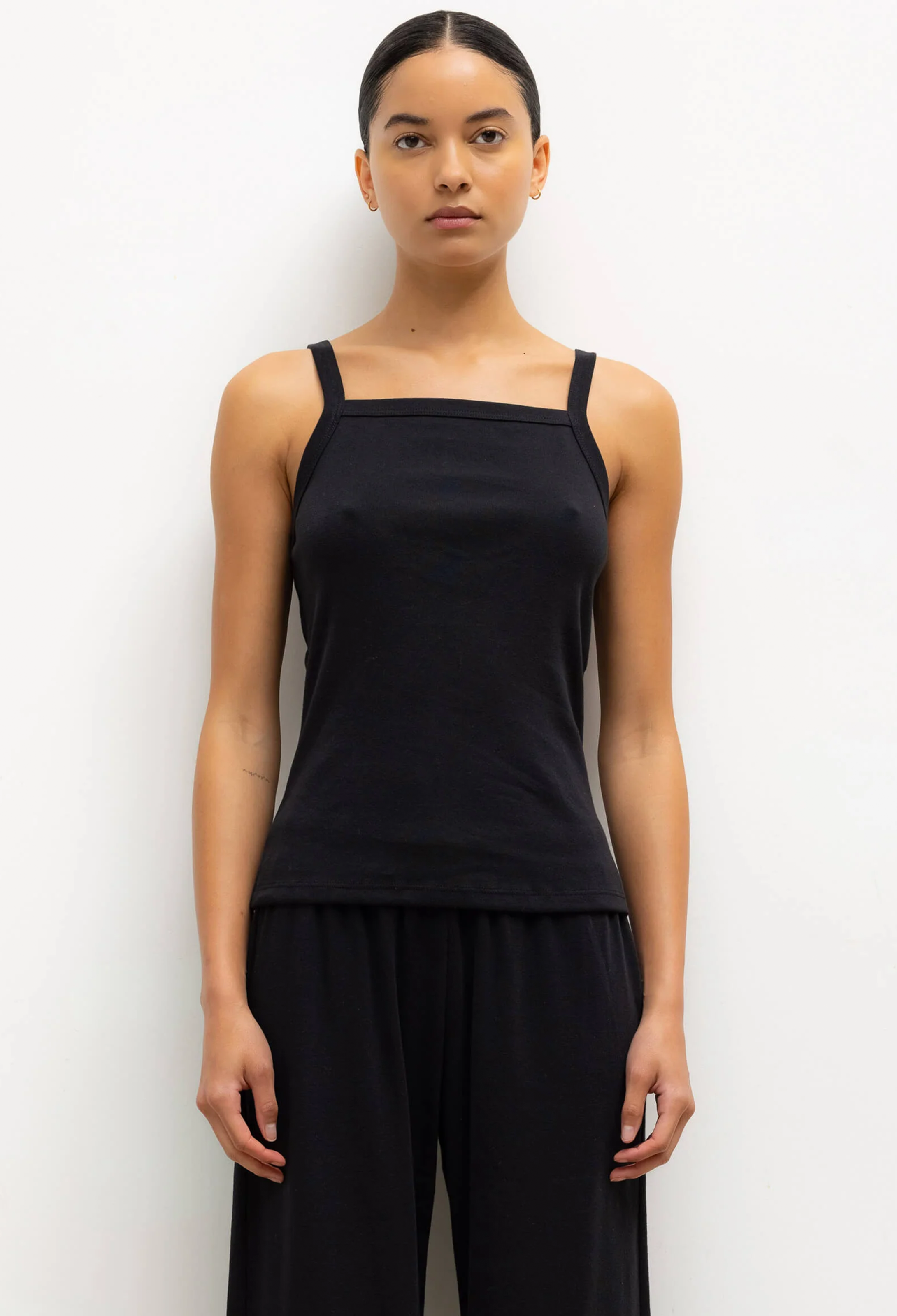 Woman wearing a black sleeveless top and black pants against a white background