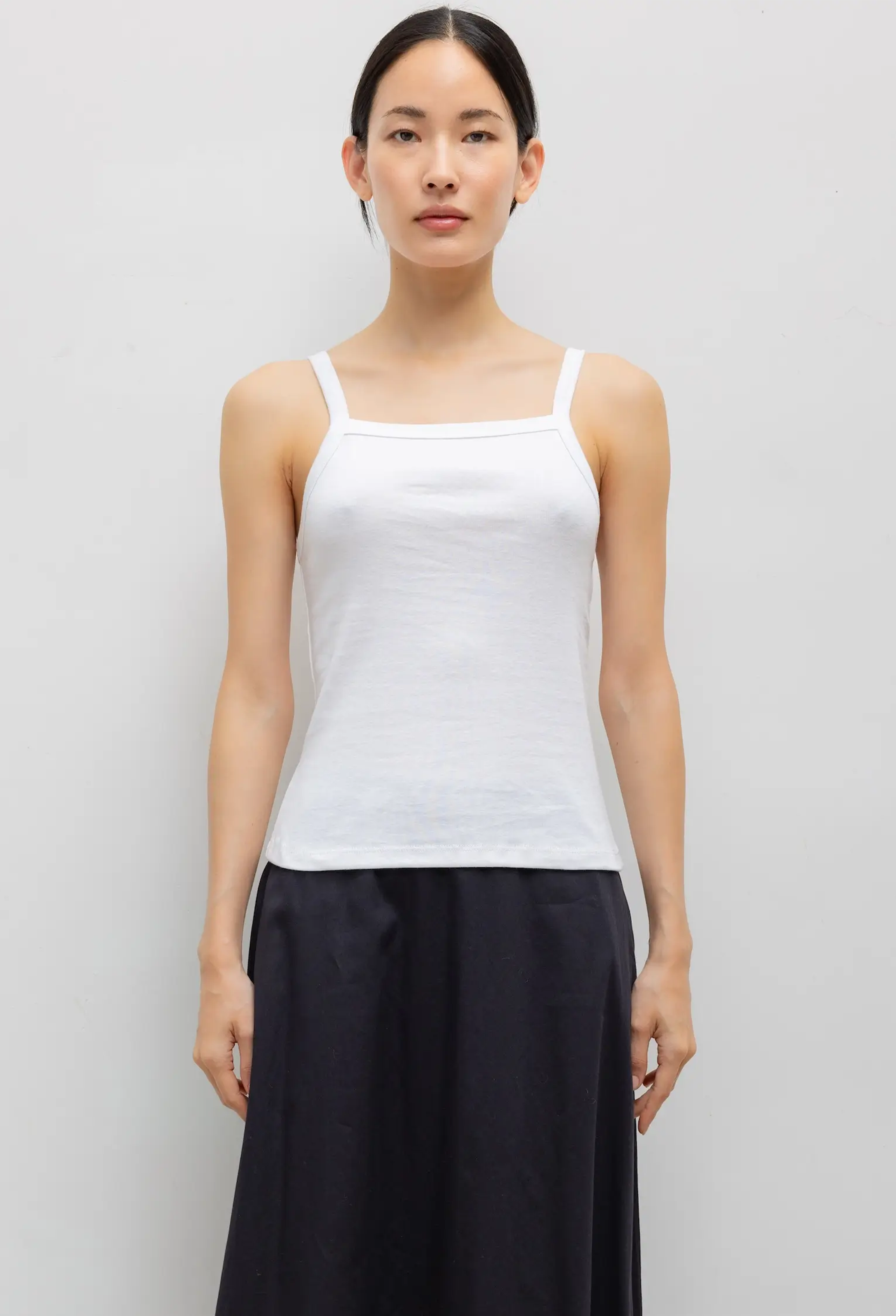 Woman wearing a white tank top and black pants on a plain background