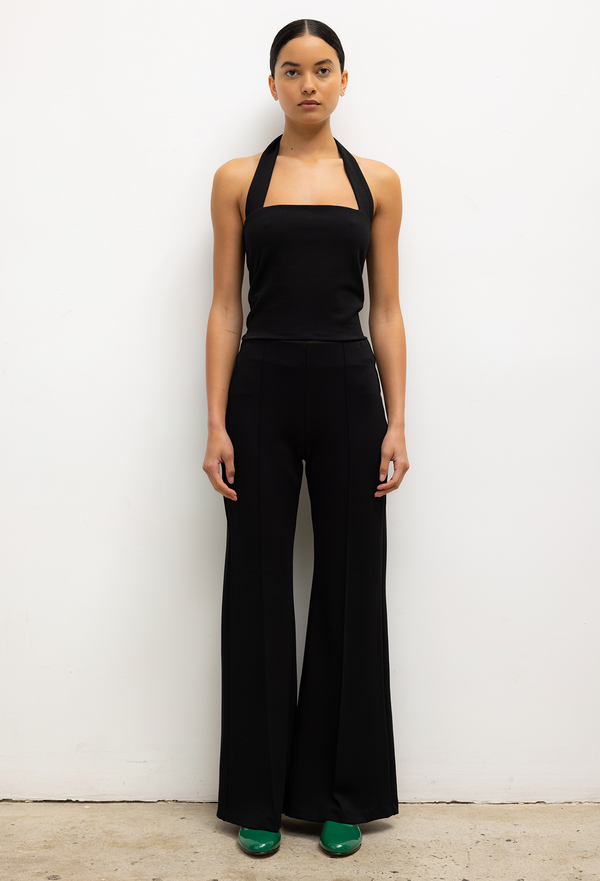 Woman wearing a black halter top and wide-leg pants against a white background