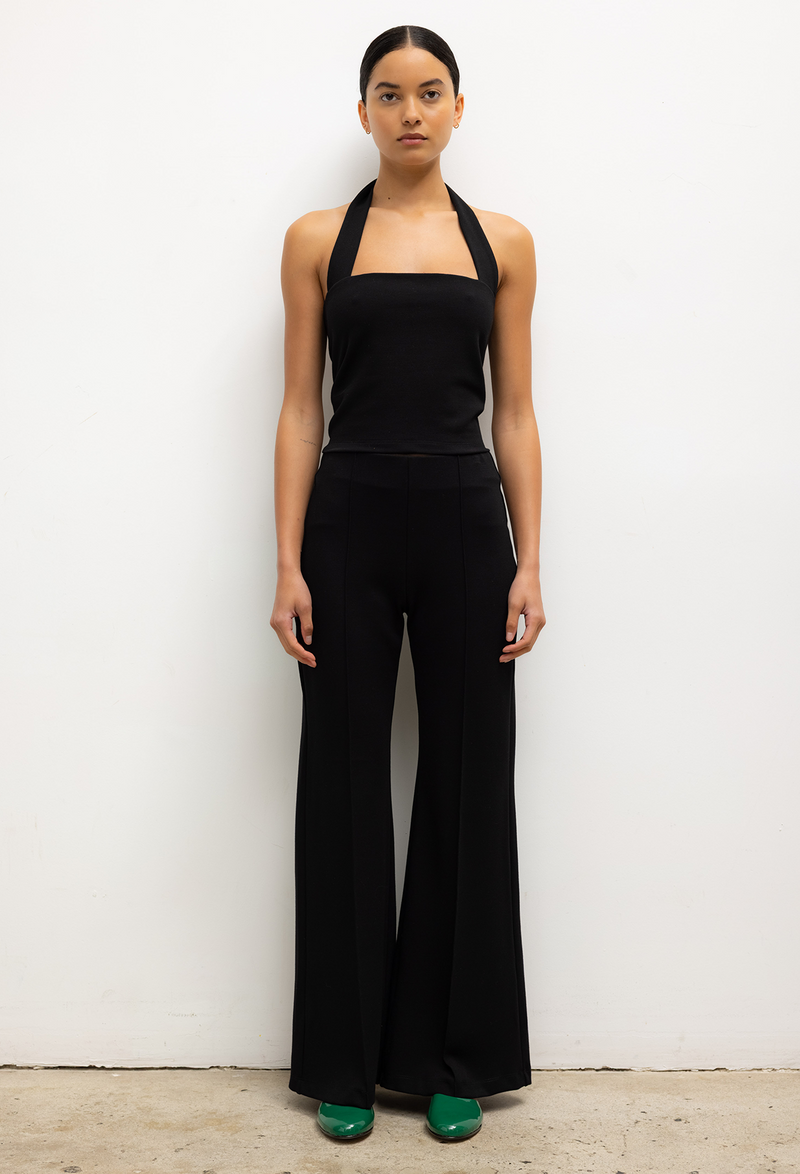 Woman wearing a black halter top and wide-leg pants against a white background